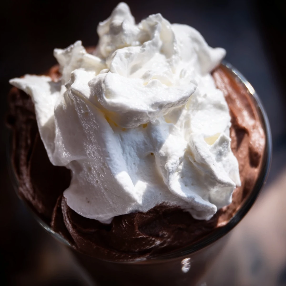 Creamy Chocolate Mousse in a glass, topped with a fluffy swirl of fresh whipped cream and chocolate shavings for an indulgent dessert.