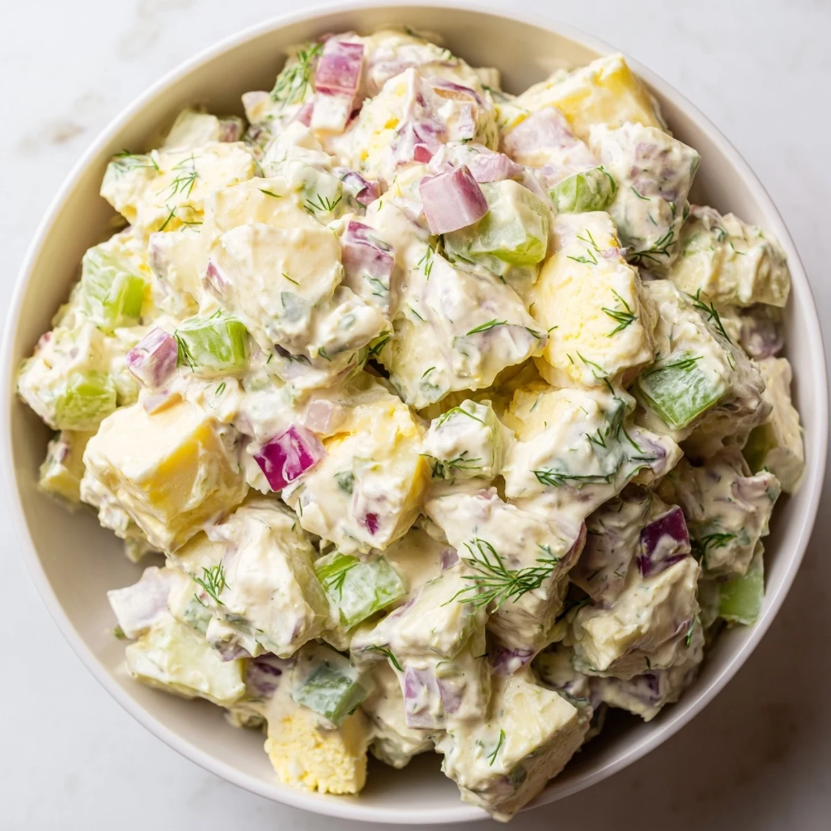 Spoon some Creamy Potato Salad with Dill onto a plate, highlighting the creamy dressing and chopped hard-boiled eggs for a classic side.