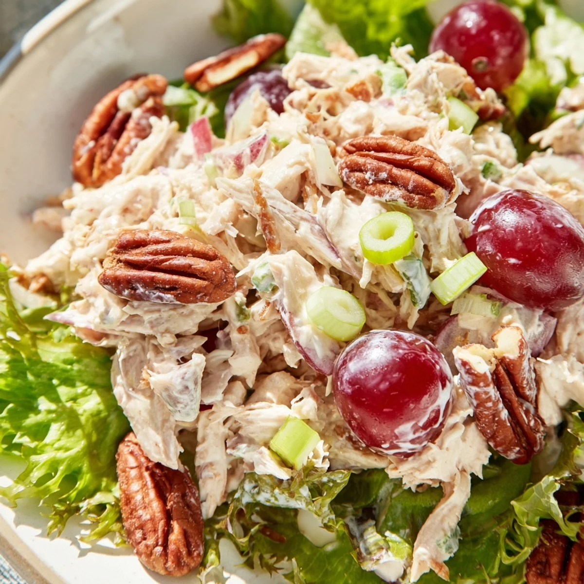A bowl of creamy Chicken Salad with Pecans, featuring tender chicken, juicy red grapes, and celery, served on crisp green lettuce.