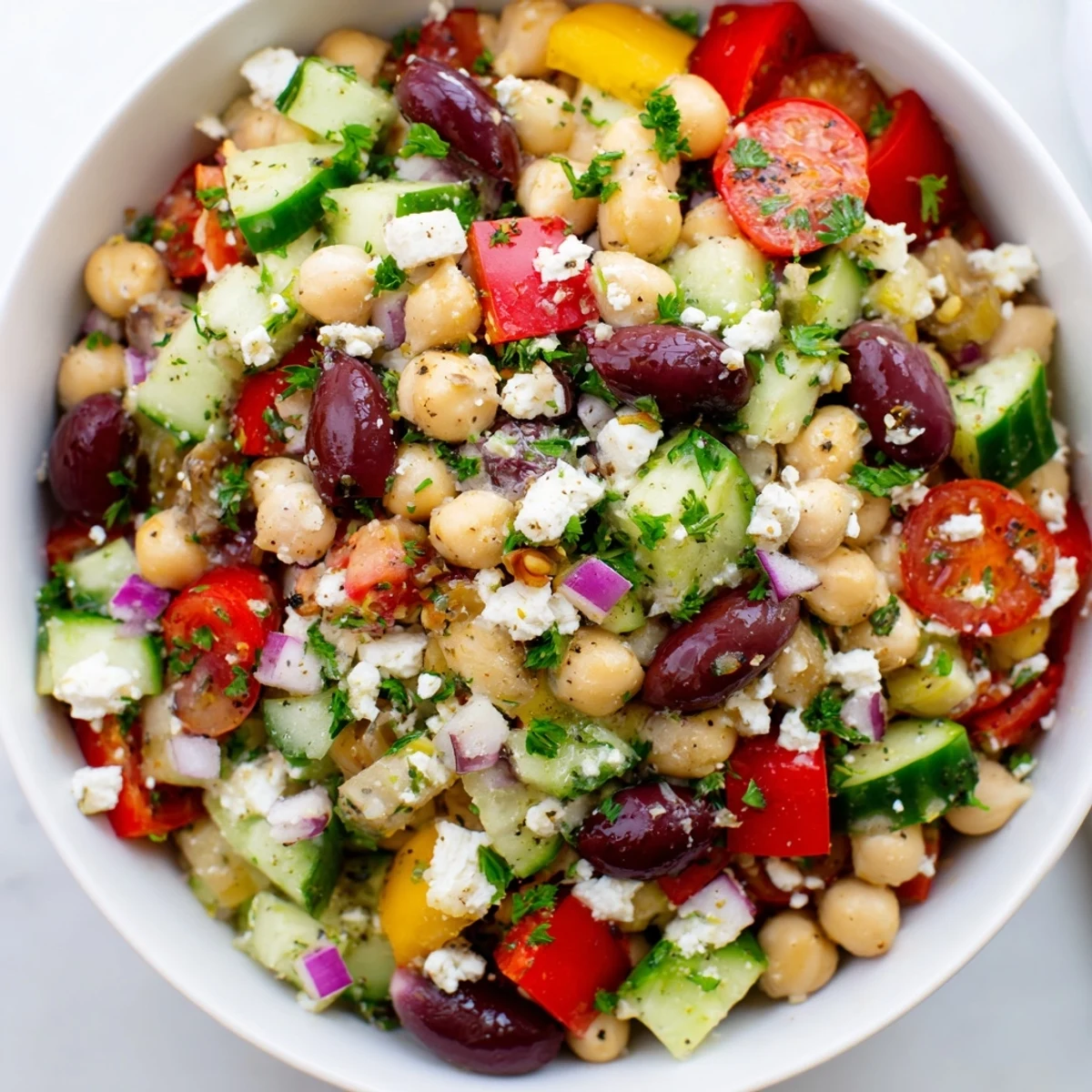 Colorful Mediterranean Chickpea and Feta Salad tossed with Kalamata olives and parsley, showcasing vibrant red onions and fresh vegetables on a rustic table.