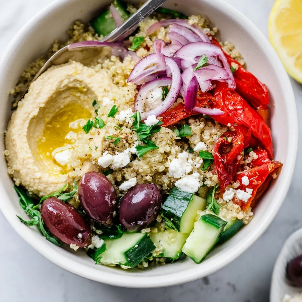 A vibrant Mediterranean Quinoa Bowl topped with creamy hummus, feta, and fresh veggies on a white plate.