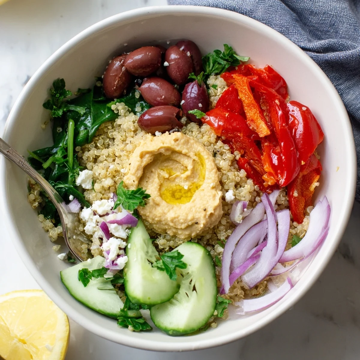 Serving suggestion for a Mediterranean Quinoa Bowl with a generous scoop of hummus and a lemon wedge.