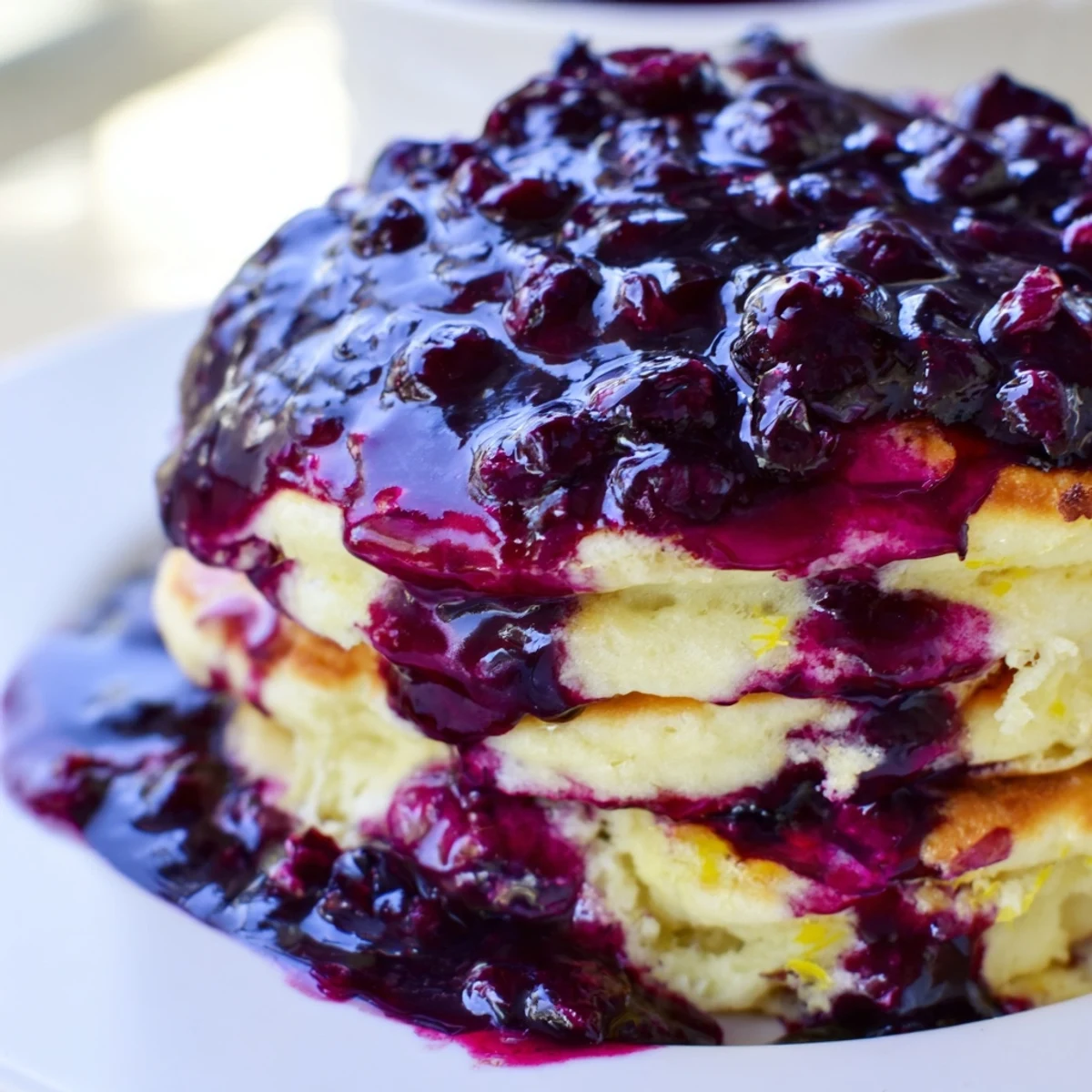 Golden, fluffy Lemon Ricotta Pancakes stacked high and generously drizzled with warm blueberry syrup for a sweet morning treat.