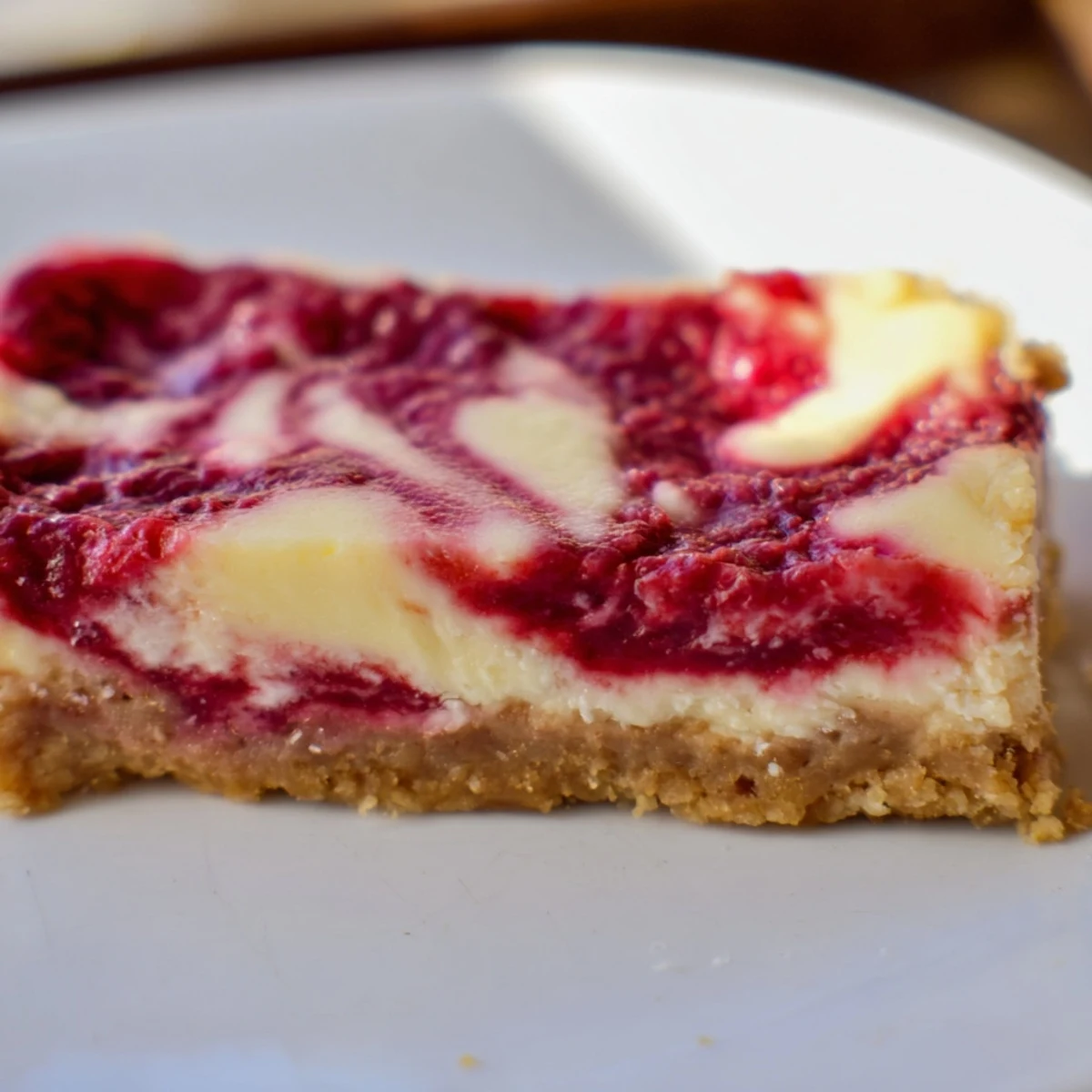 A close-up slice reveals creamy white chocolate cheesecake filling swirled with vibrant tangy raspberry sauce. 