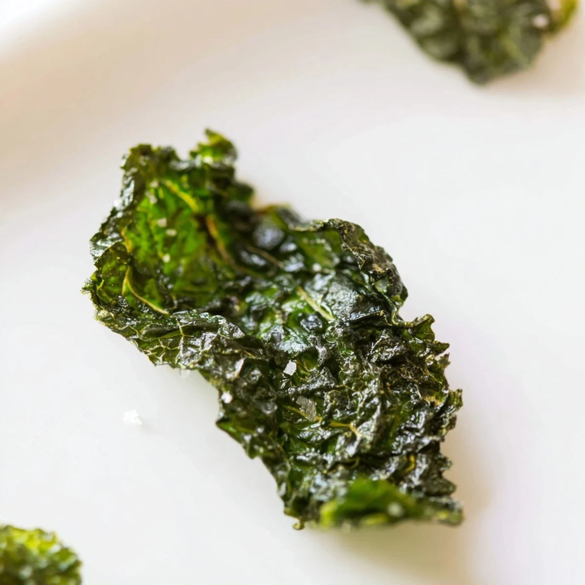 Vibrant green kale chips lightly coated in olive oil and sea salt, arranged on a parchment-lined tray for a healthy snack.  