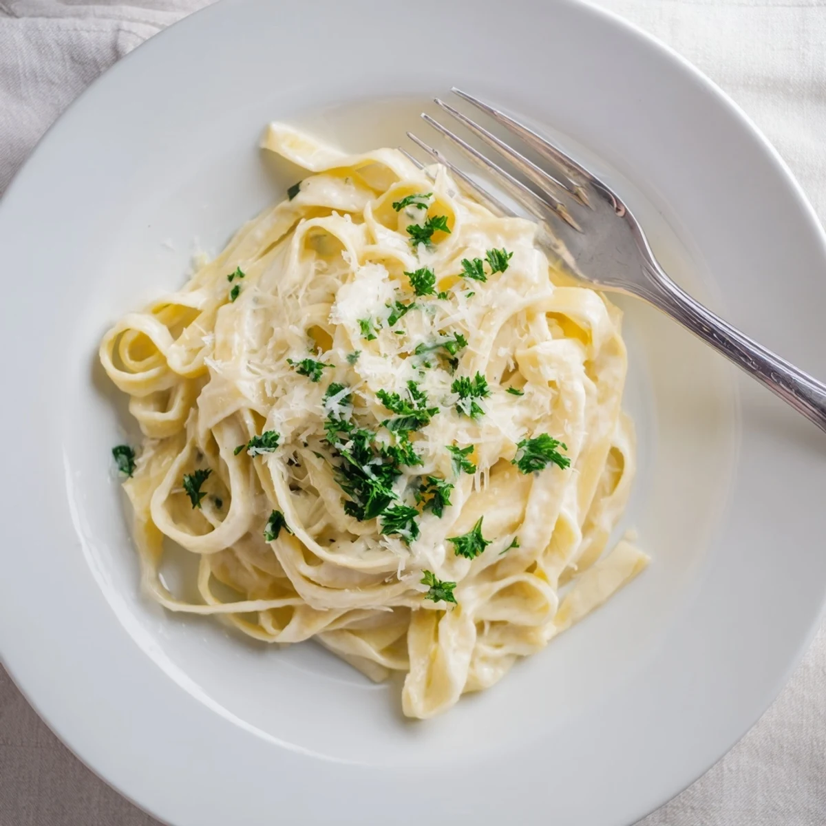 A close-up of creamy dinner pasta sauce coating fettuccine, garnished with fresh parsley and Parmesan cheese.  
