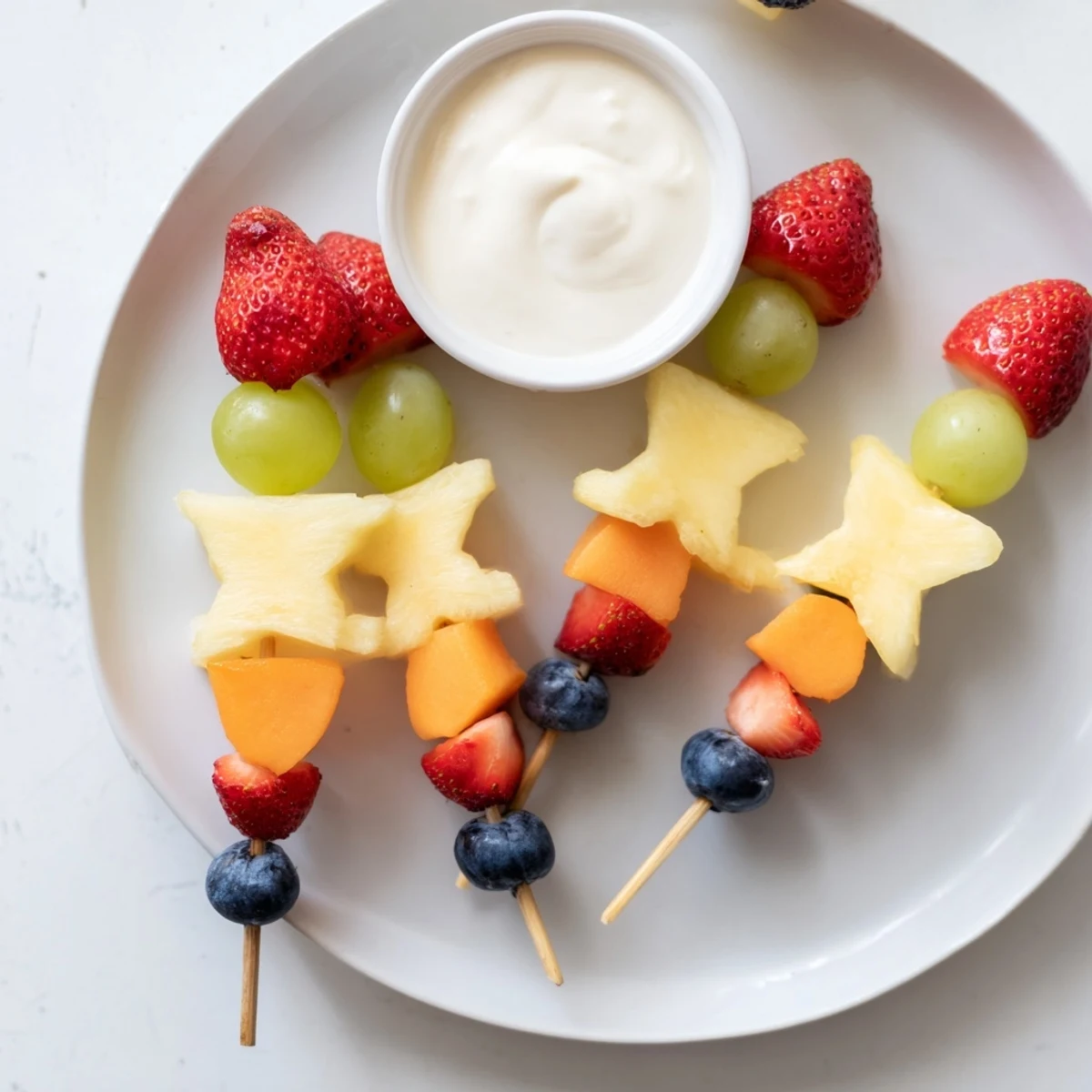 Sweetheart Fruit Kabobs with Yogurt are artfully arranged with vibrant strawberries, grapes, and pineapple on a platter with a creamy dip.