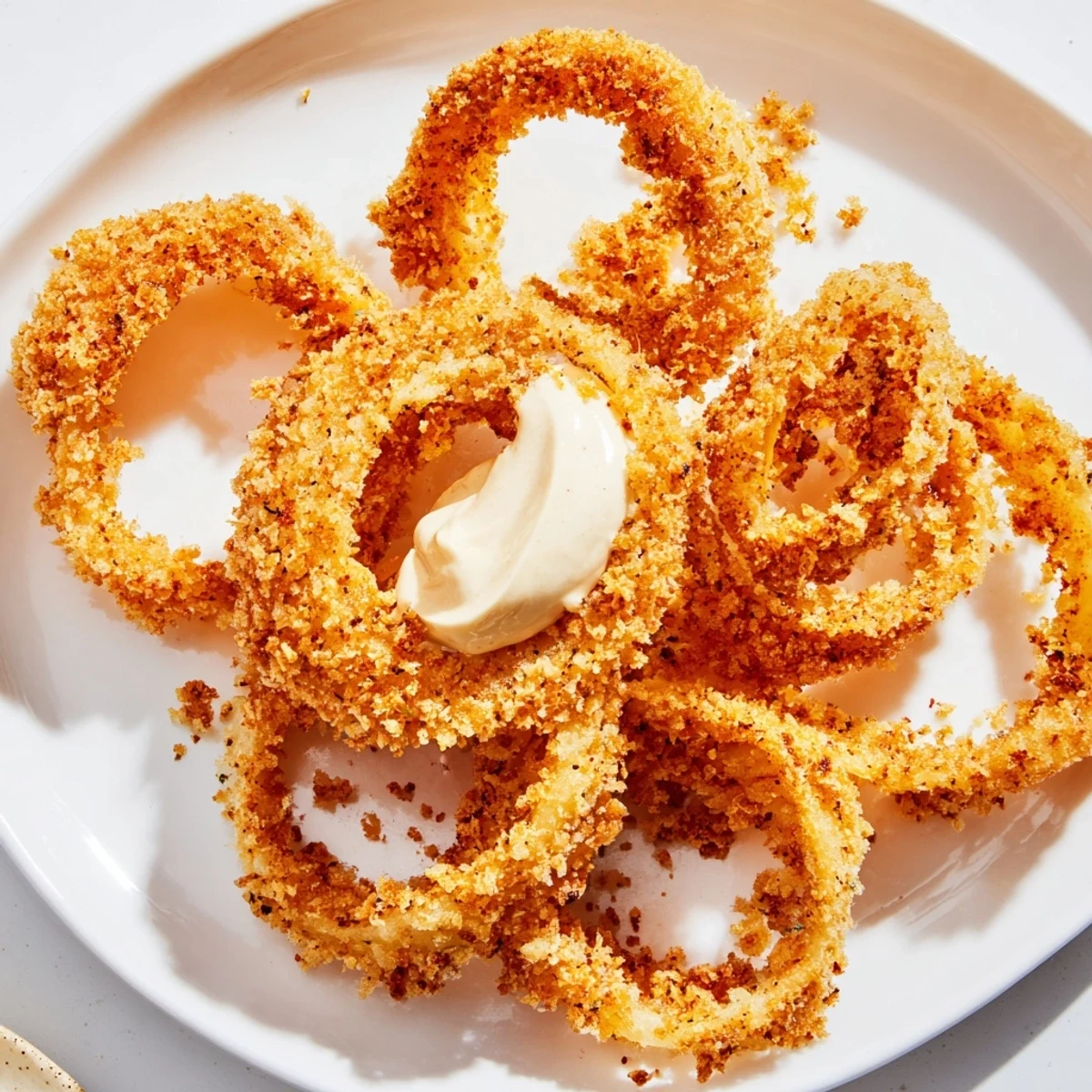 Freshly cooked air fryer onion rings with a golden panko crust sit beside creamy chipotle mayo for dipping. 