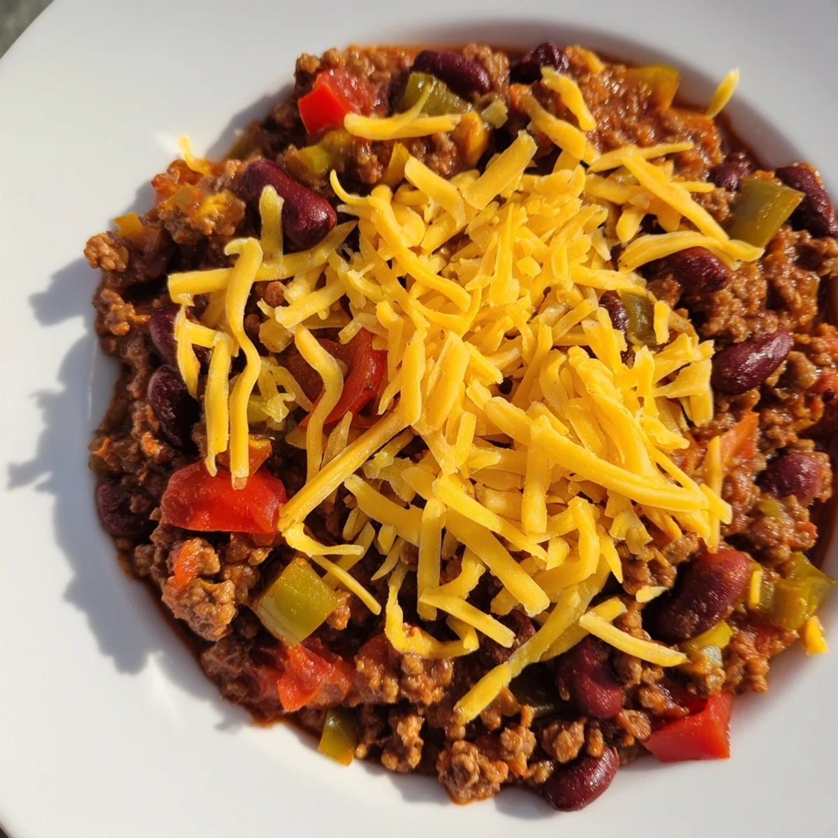 A steaming bowl of Beef and Bean Chili with Cheddar Cheese topped with melted cheese and green onions.