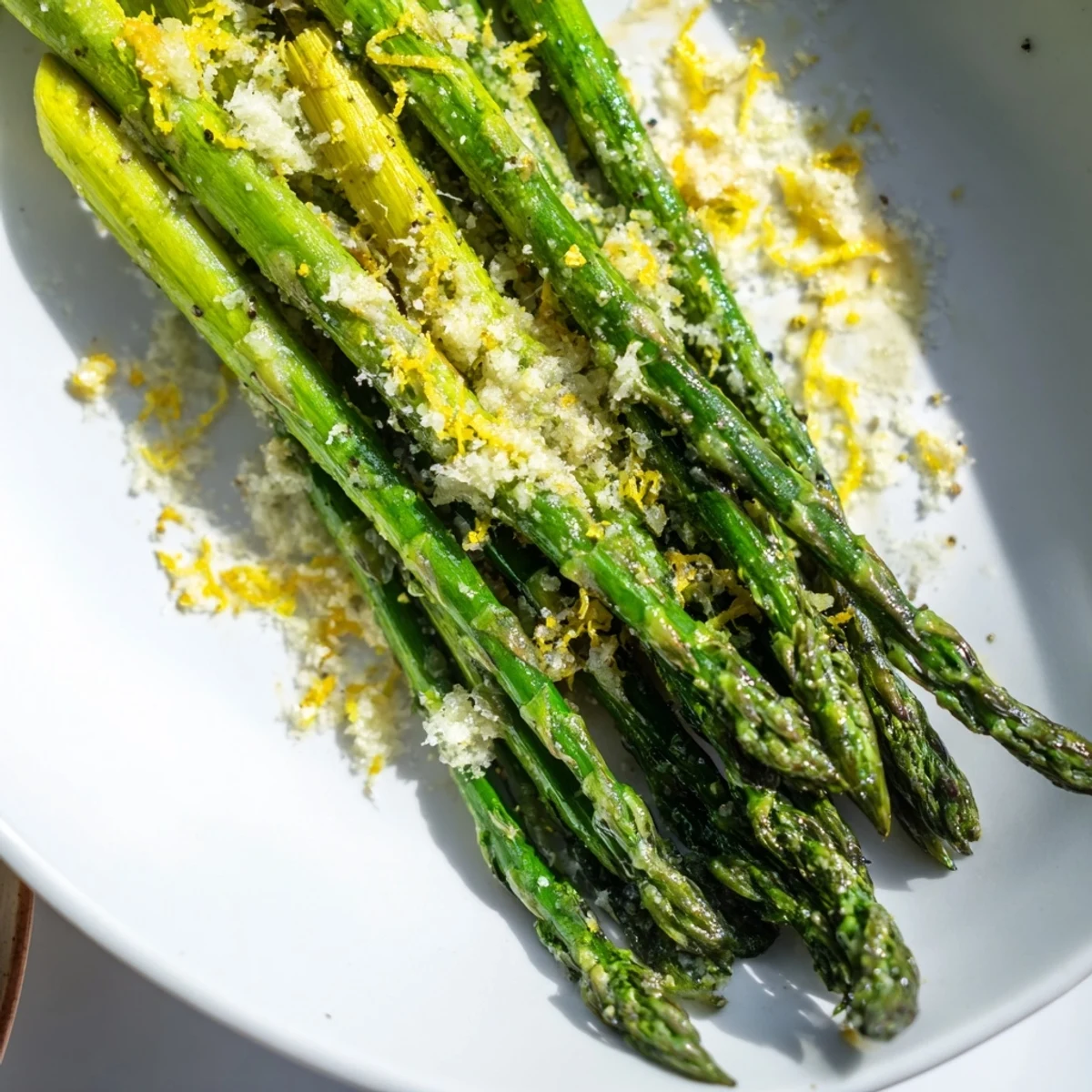 Close-up of roasted asparagus with Parmesan and lemon zest, garnished with fresh parsley on a baking sheet.