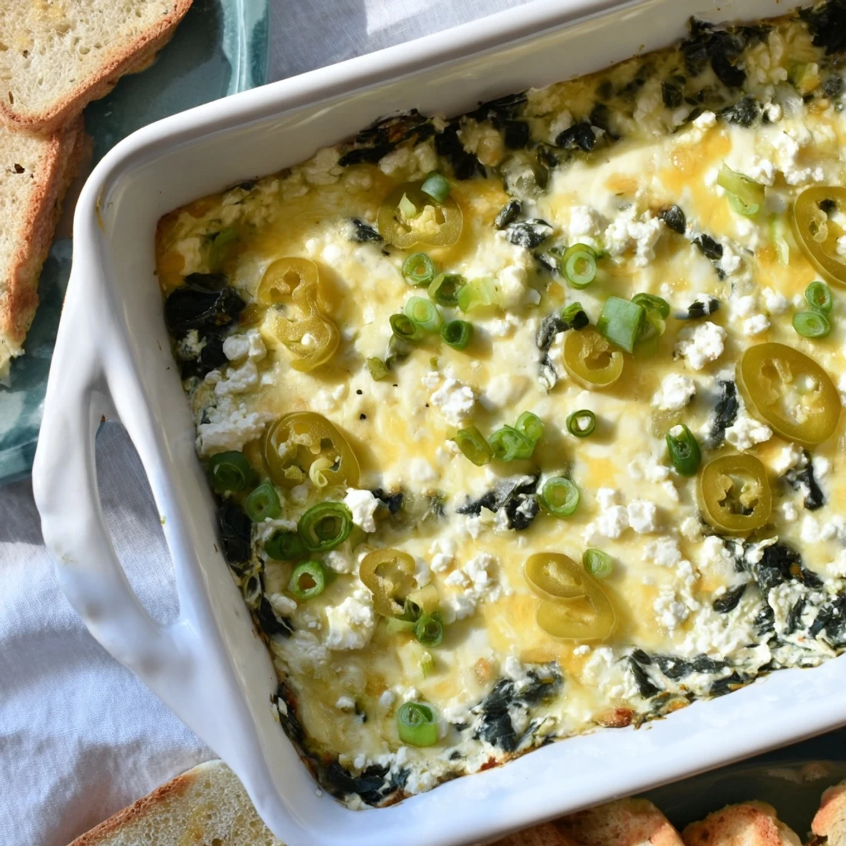 In a serving dish, the warm Spinach and Pepperoncini Baked Feta Dip is surrounded by crunchy pita chips for dipping.