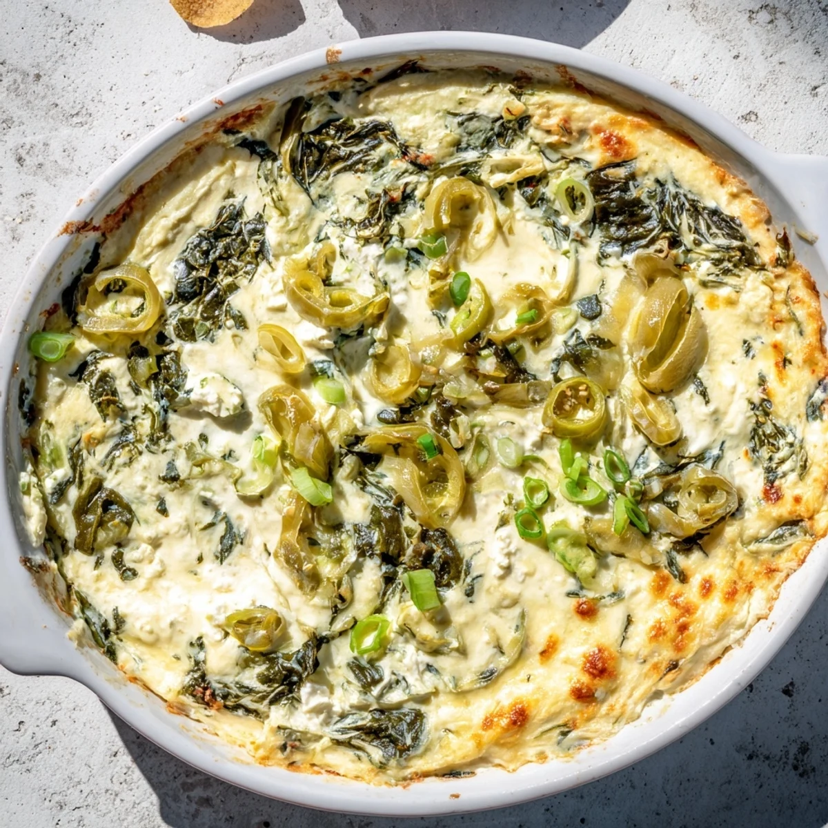 A golden, creamy skillet of Spinach and Pepperoncini Baked Feta Dip garnished with herbs and sliced pepperoncini.