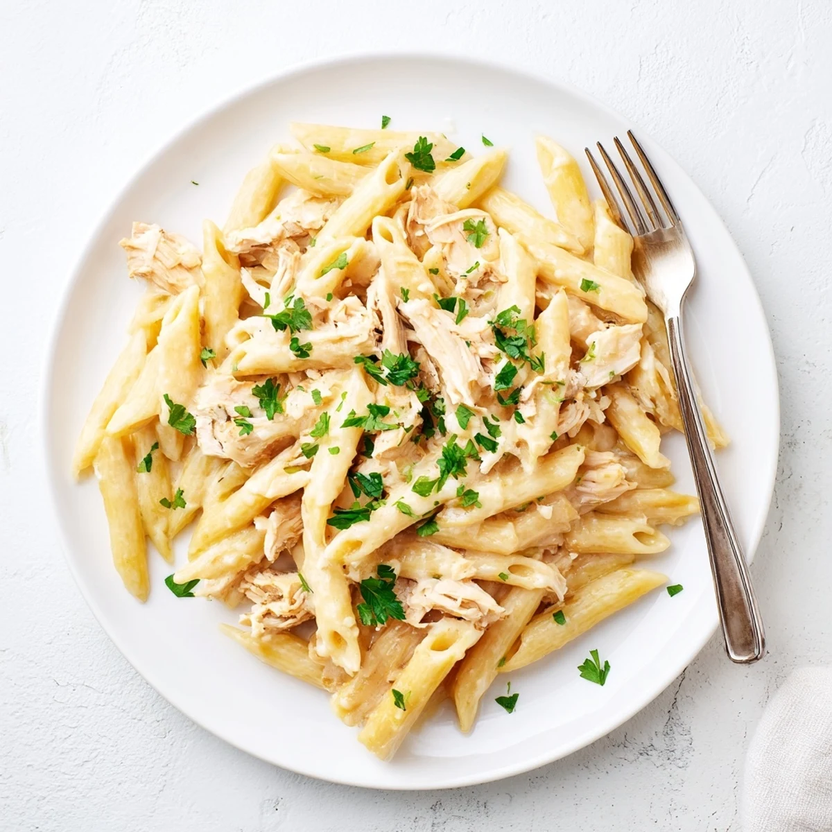 Warm Crockpot Garlic Parmesan Chicken Pasta served in a white bowl with a garnish.