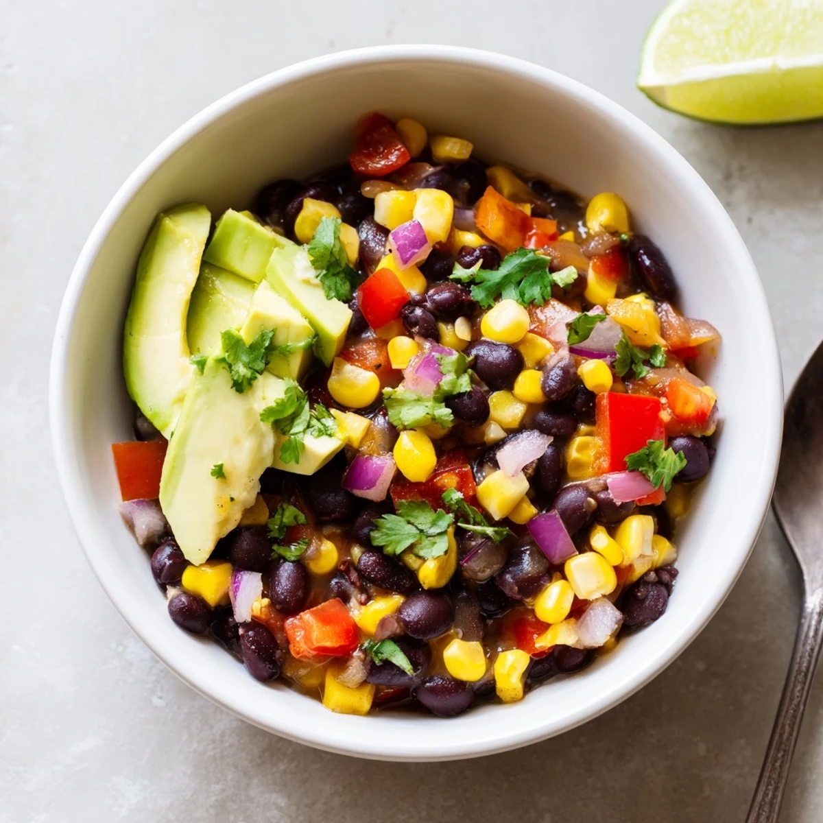 A vibrant serving of Black Bean Corn Chili Lime Delight topped with sliced avocado and cilantro.