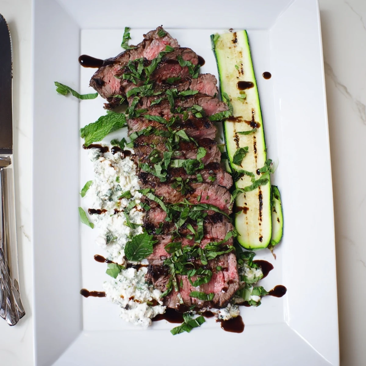 Sizzling balsamic flank steak just off the grill, paired with tender grilled zucchini and whipped feta spread on a wooden board.