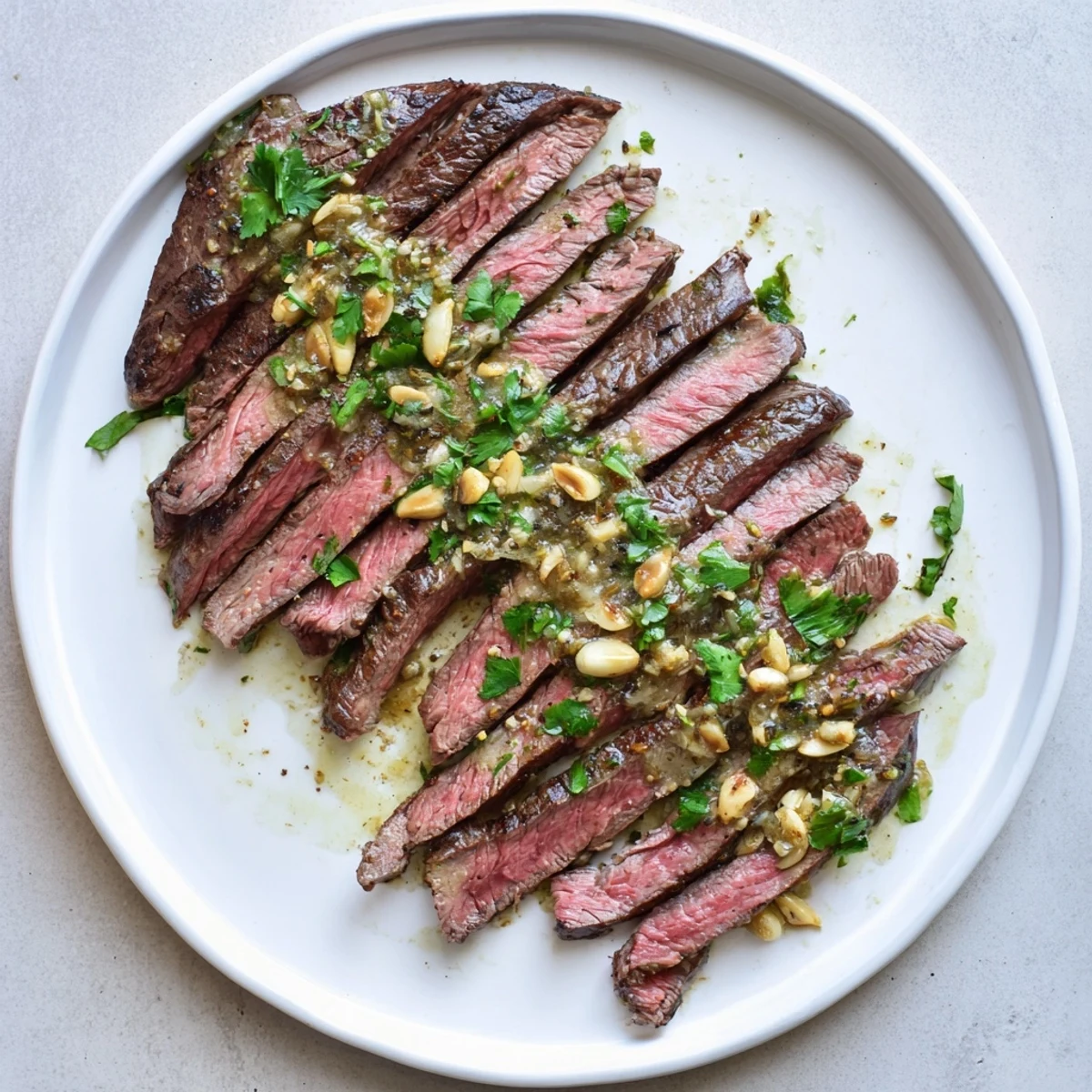Sliced flank steak drizzled with velvety roasted garlic sauce, garnished with fresh parsley for a special dinner.