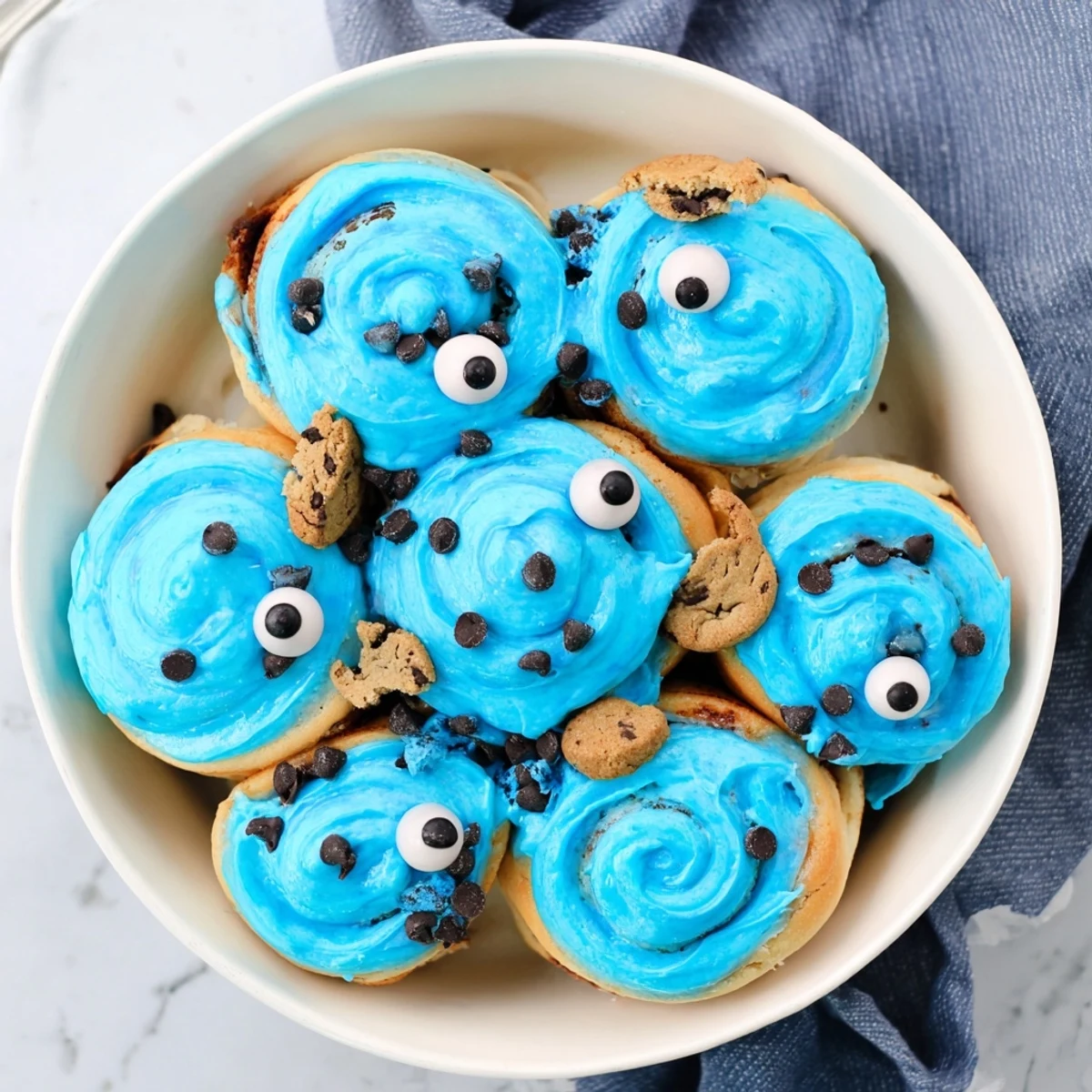 Warm blue Cookie Monster Cinnamon Rolls with chocolate chip filling, decorated with candy eyes and mini cookie halves.