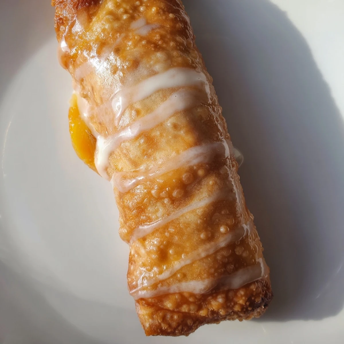 Golden peach cobbler egg rolls drizzled with vanilla glaze on a white plate