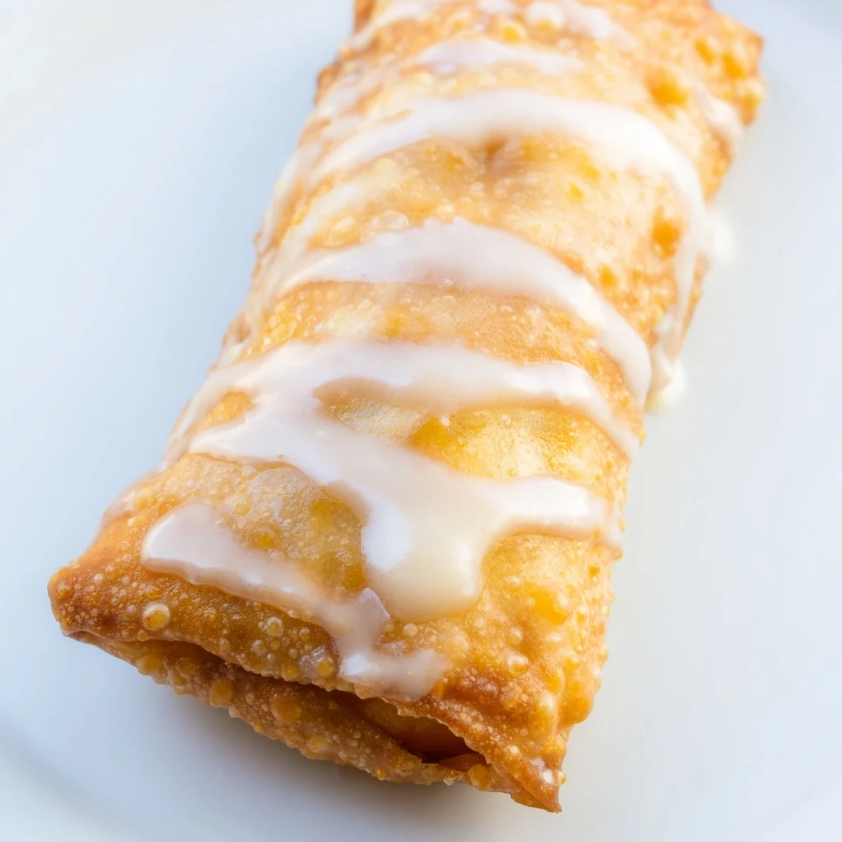 Crispy fried egg rolls stuffed with cinnamon spiced peaches and sweet vanilla icing
