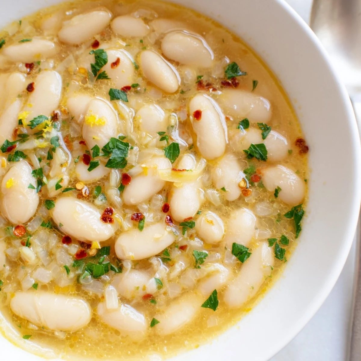 Steaming bowl of miso butter brothy beans topped with vibrant parsley and lemon zest