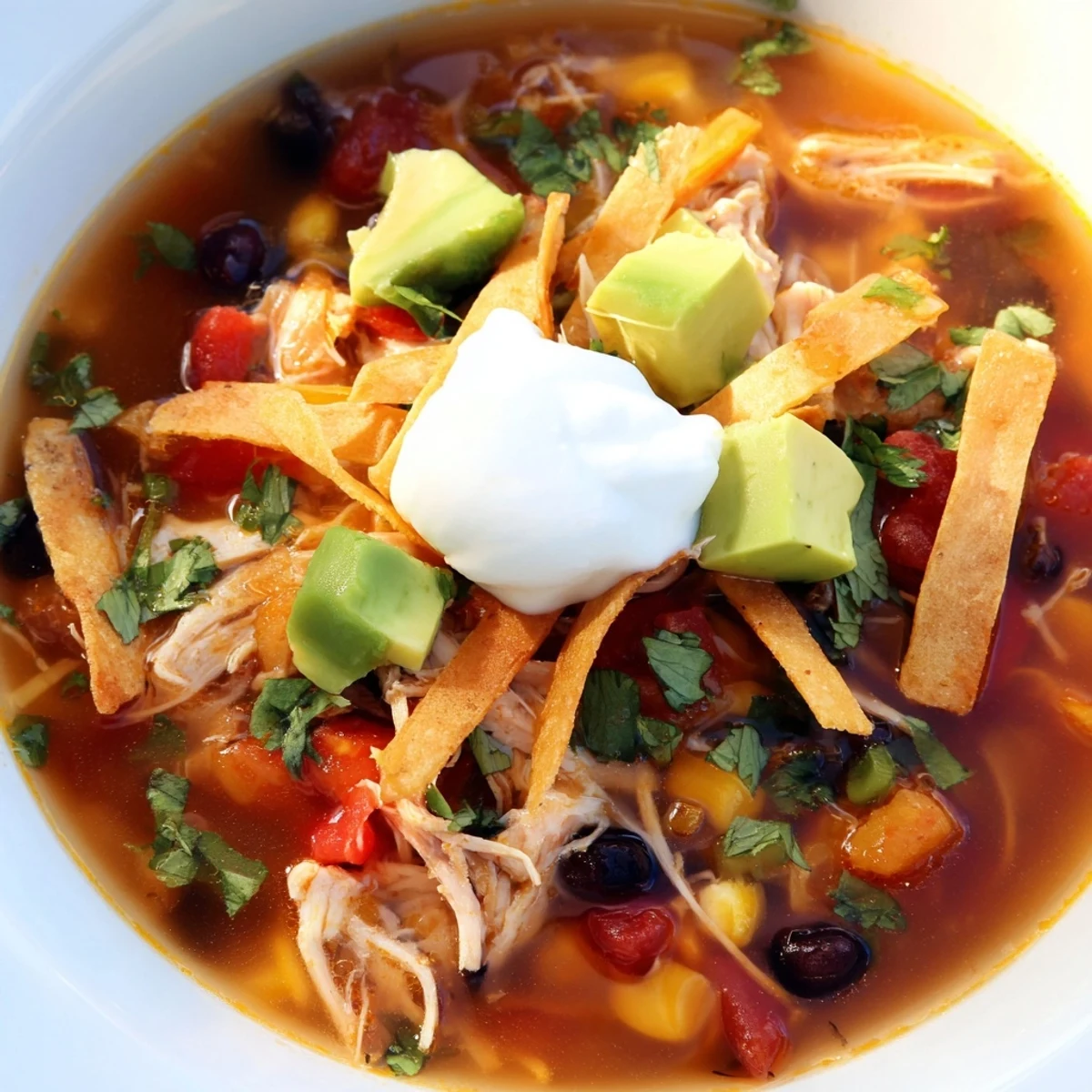 Hearty classic chicken tortilla soup garnished with creamy avocado, shredded cheese, and zesty lime wedges