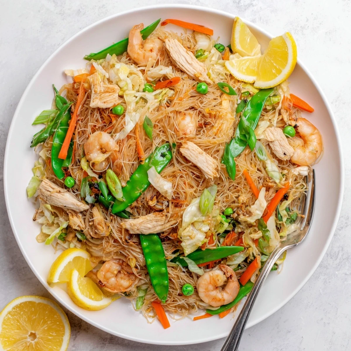 Golden bowl of traditional Pancit Bihon topped with tender chicken, plump shrimp, and crisp colorful vegetables