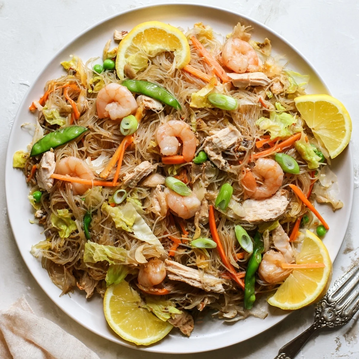 Steaming plate of savory Pancit Bihon noodle stir-fry garnished with fresh scallions and lemon wedges