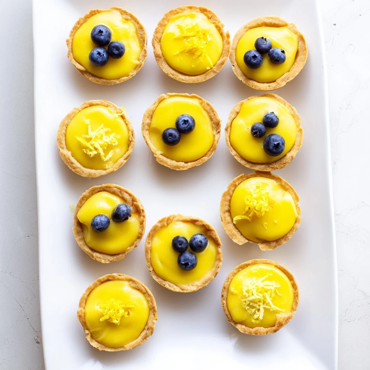 Mini tartlets filled with tangy lemon coconut cream arranged on white plate