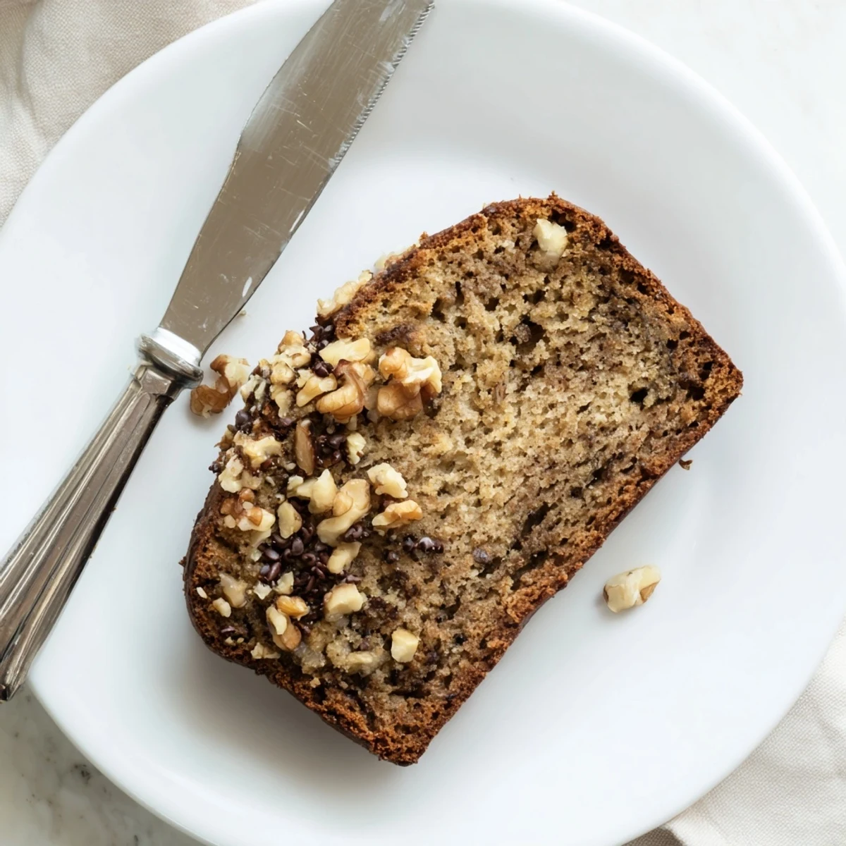 Moist best ever banana bread with walnuts served warm on a white plate