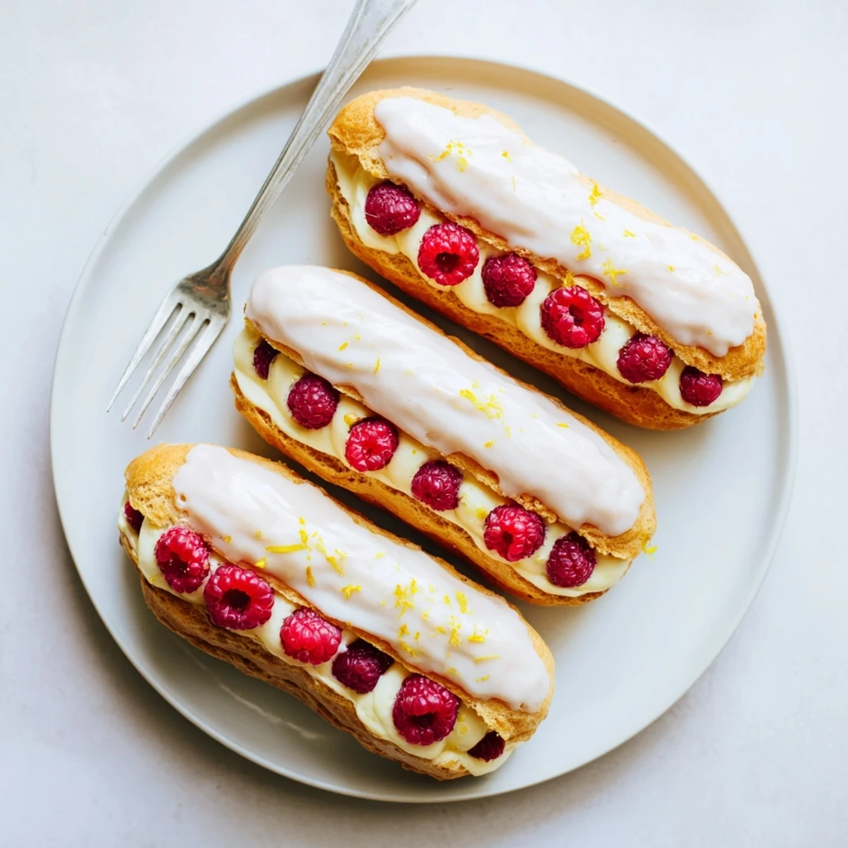 Golden lemon raspberry éclairs with light lemon glaze on a white serving plate