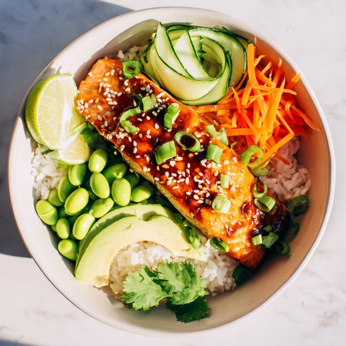 Colorful honey glazed salmon bowl arranged with crunchy cucumber carrots and edamame garnished with sesame seeds and green onions