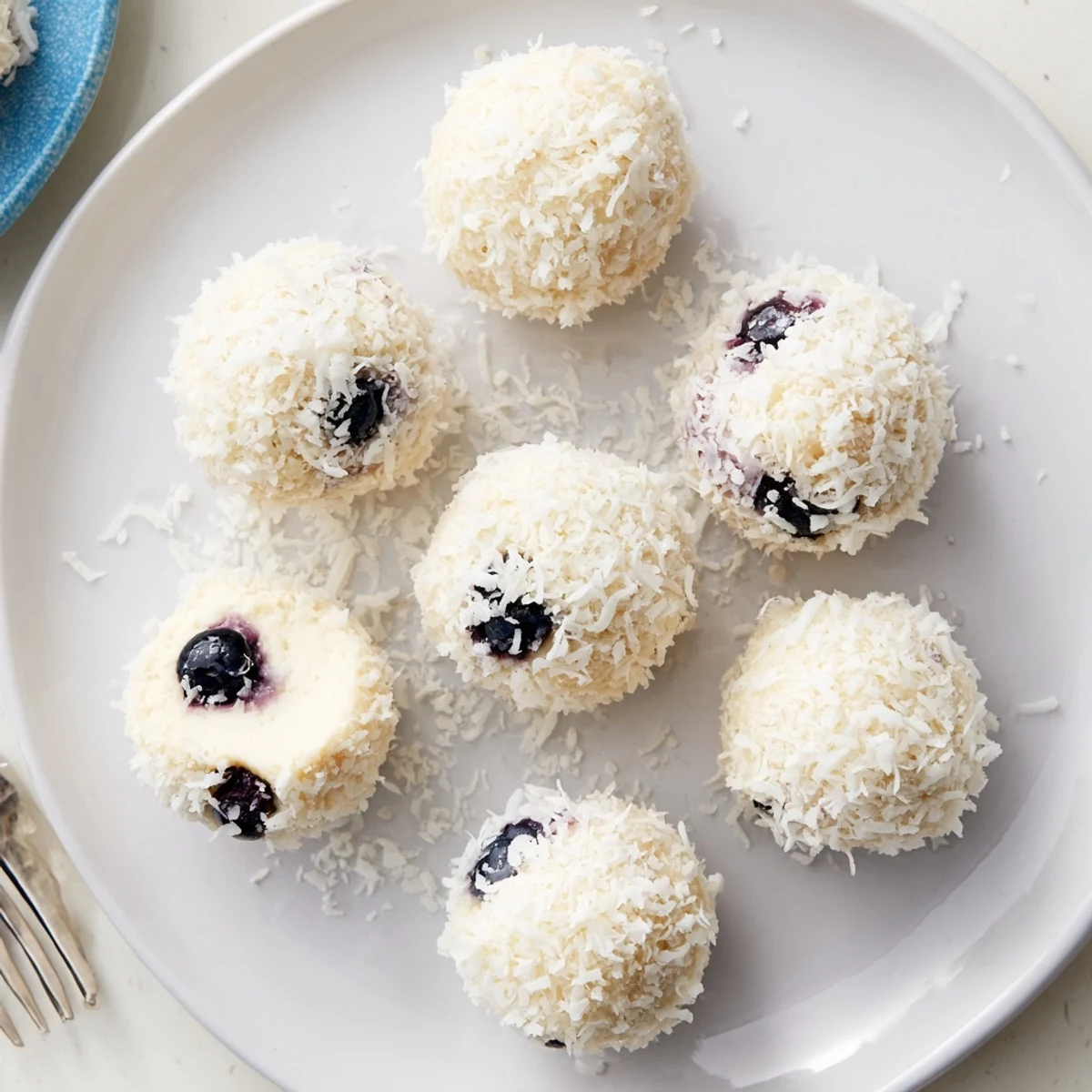 Fresh blueberry cheesecake protein bites arranged on a white plate with coconut coating