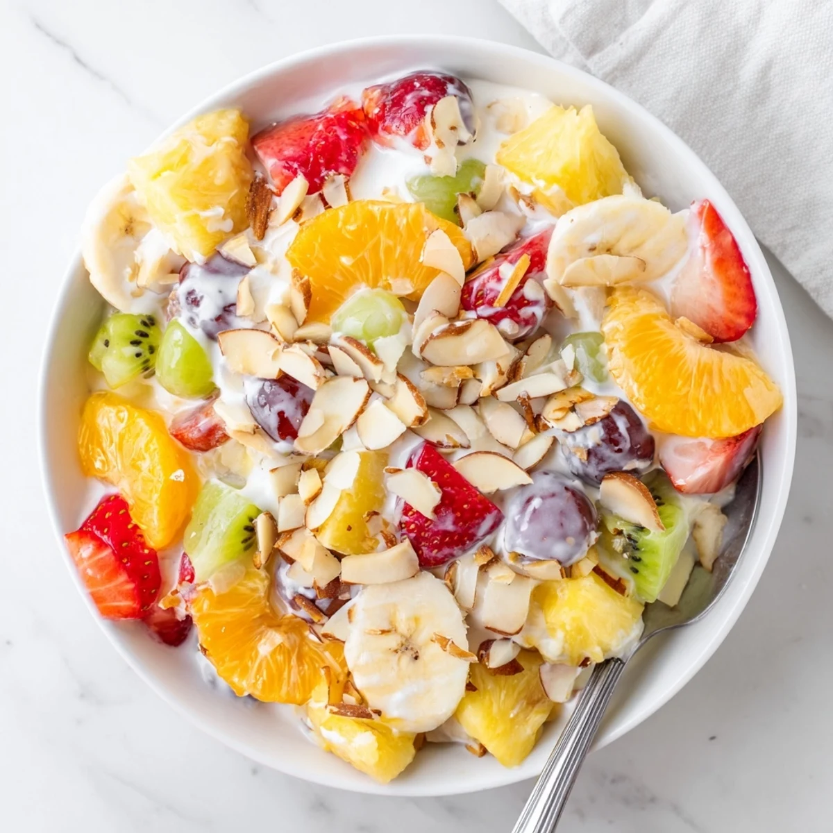 Luscious creamy fruit salad dessert topped with coconut and toasted almonds over tangy Greek yogurt dressing