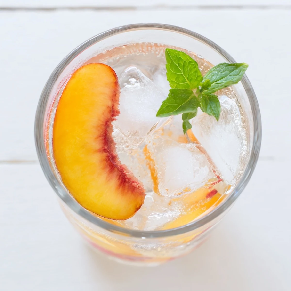 Ginger Peach Sparkler drink with floating peach slices and mint sprig in ice-filled glass