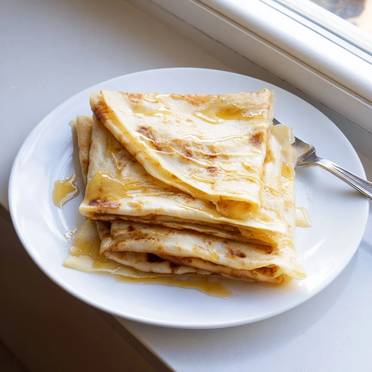 Golden brown Meloui Moroccan pancakes stacked on a rustic serving plate with honey drizzled over the flaky layered surface