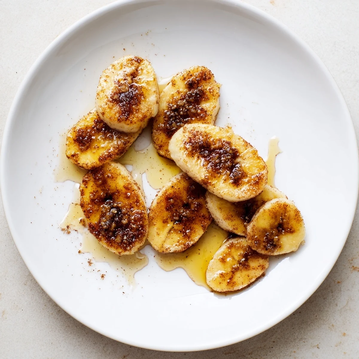 Pan fried cinnamon bananas arranged on a white plate with golden caramelized coating