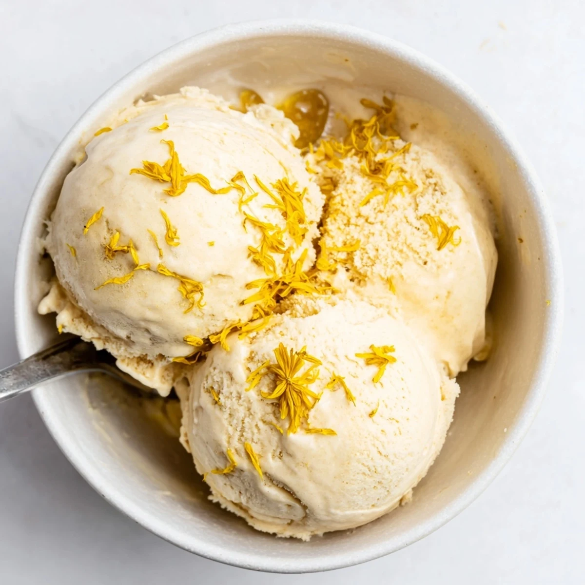 Smooth floral honey ice cream garnished with edible dandelion blossoms on white plate