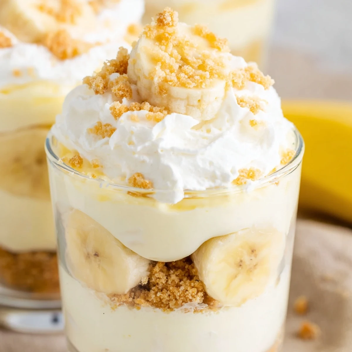 Creamy no bake banana pudding cheesecake cups with fresh banana slices and vanilla wafer crumbs on top