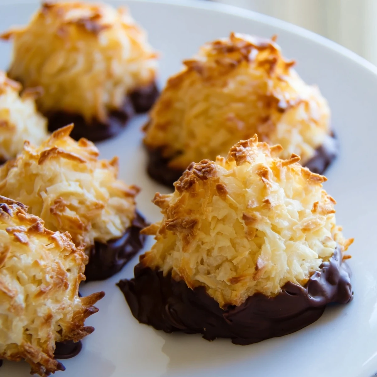Chewy coconut macaroons dipped in rich melted chocolate on a rustic wooden board