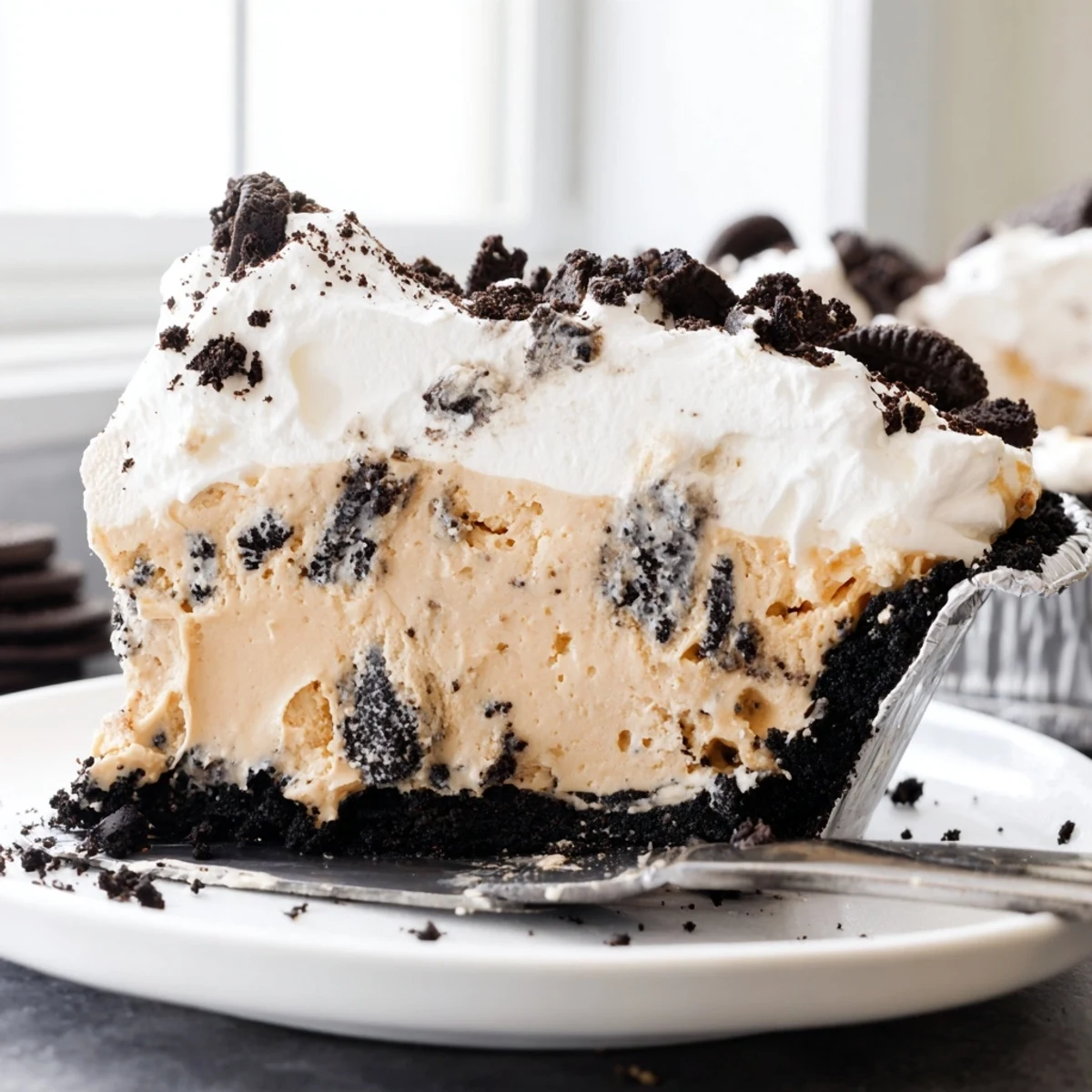 Creamy peanut butter Oreo pie sliced thick with billowy whipped cream and cookie crumbles