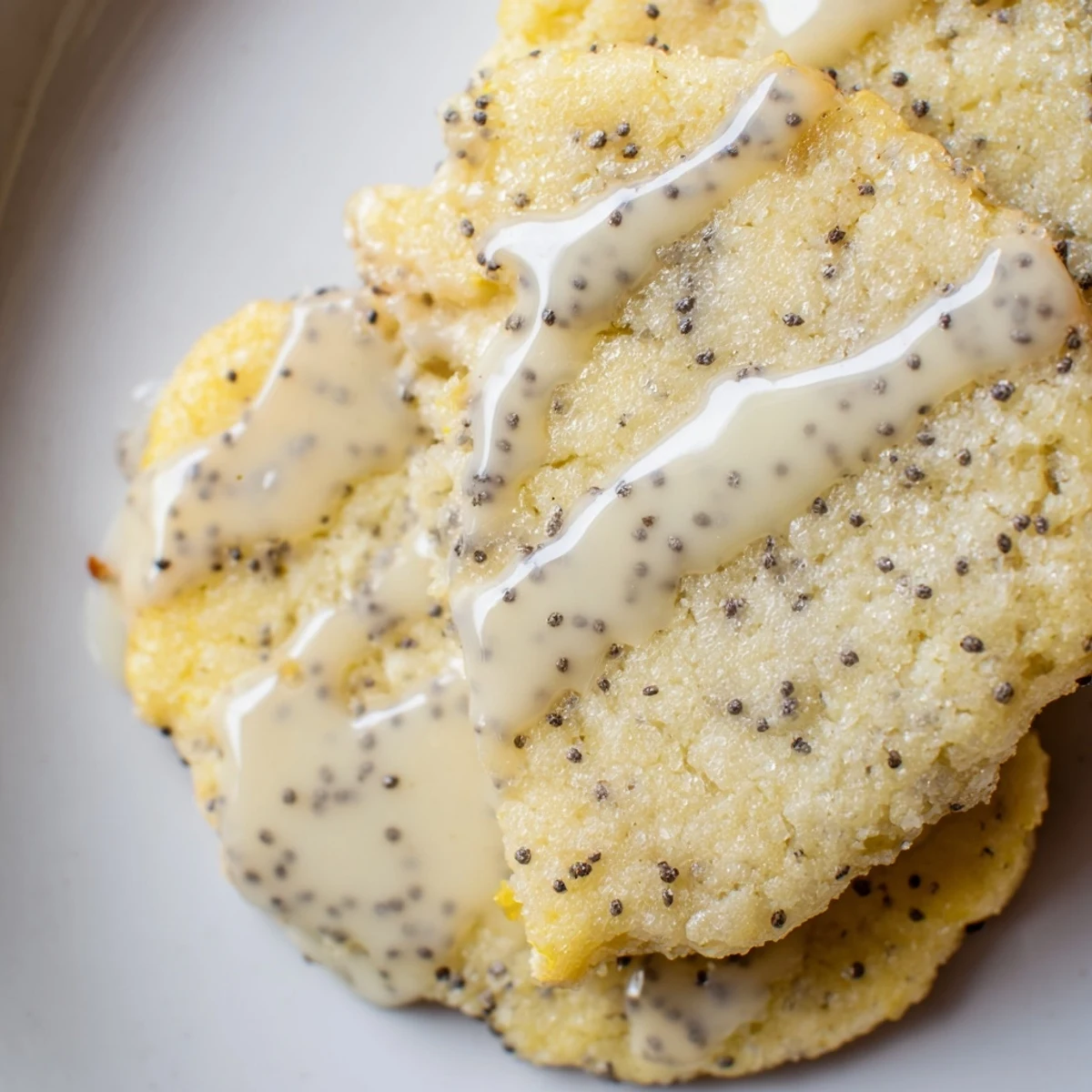 Golden lemon poppy seed cookies with crackly tops drizzled with sweet citrus glaze on a rustic white plate.