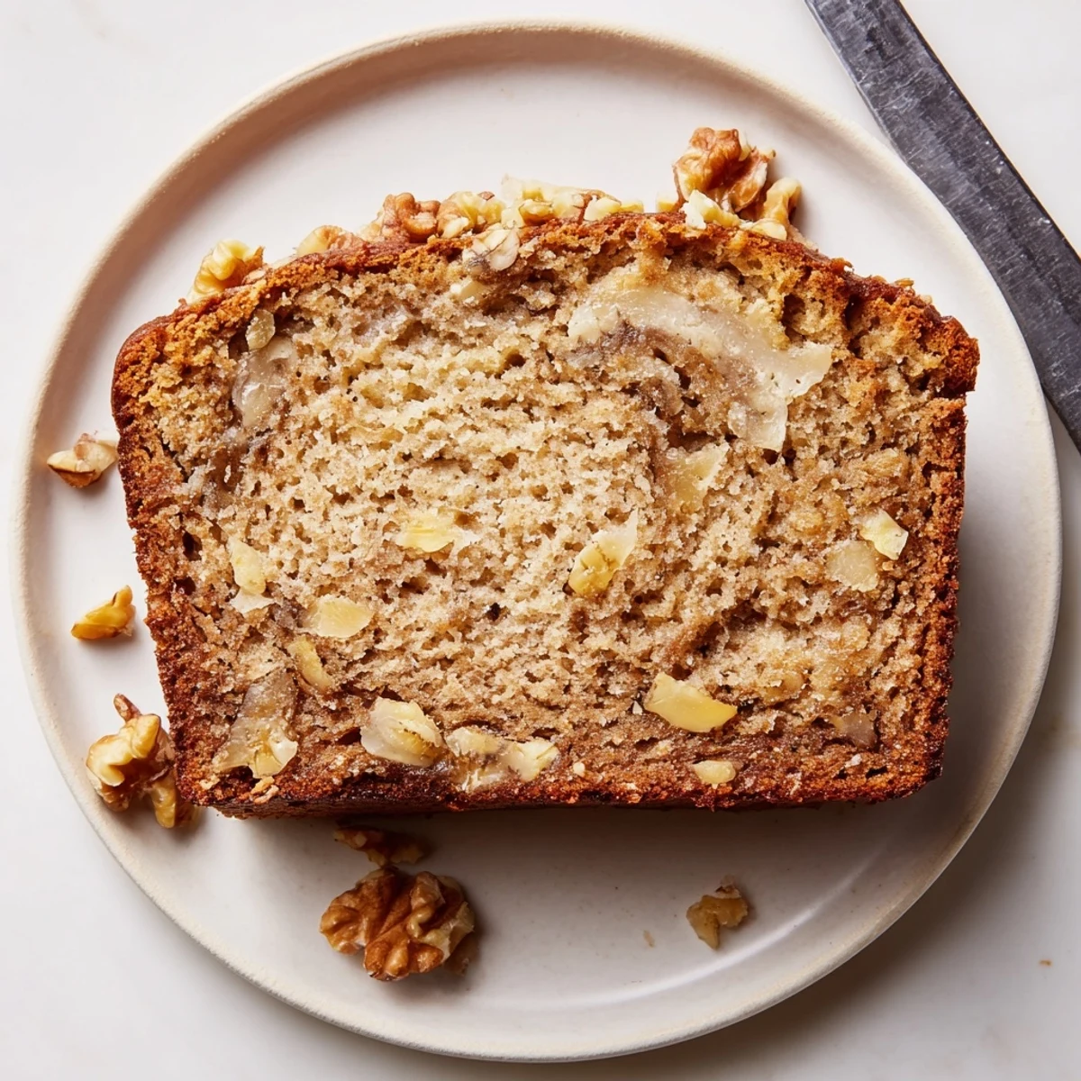 Golden banana nut bread sliced on a rustic cutting board with scattered walnuts