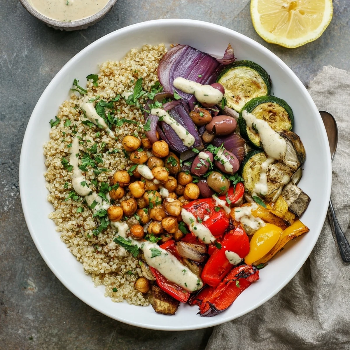 A cozy vegan Mediterranean roasted vegetables bowl served over quinoa with a zesty lemon tahini drizzle