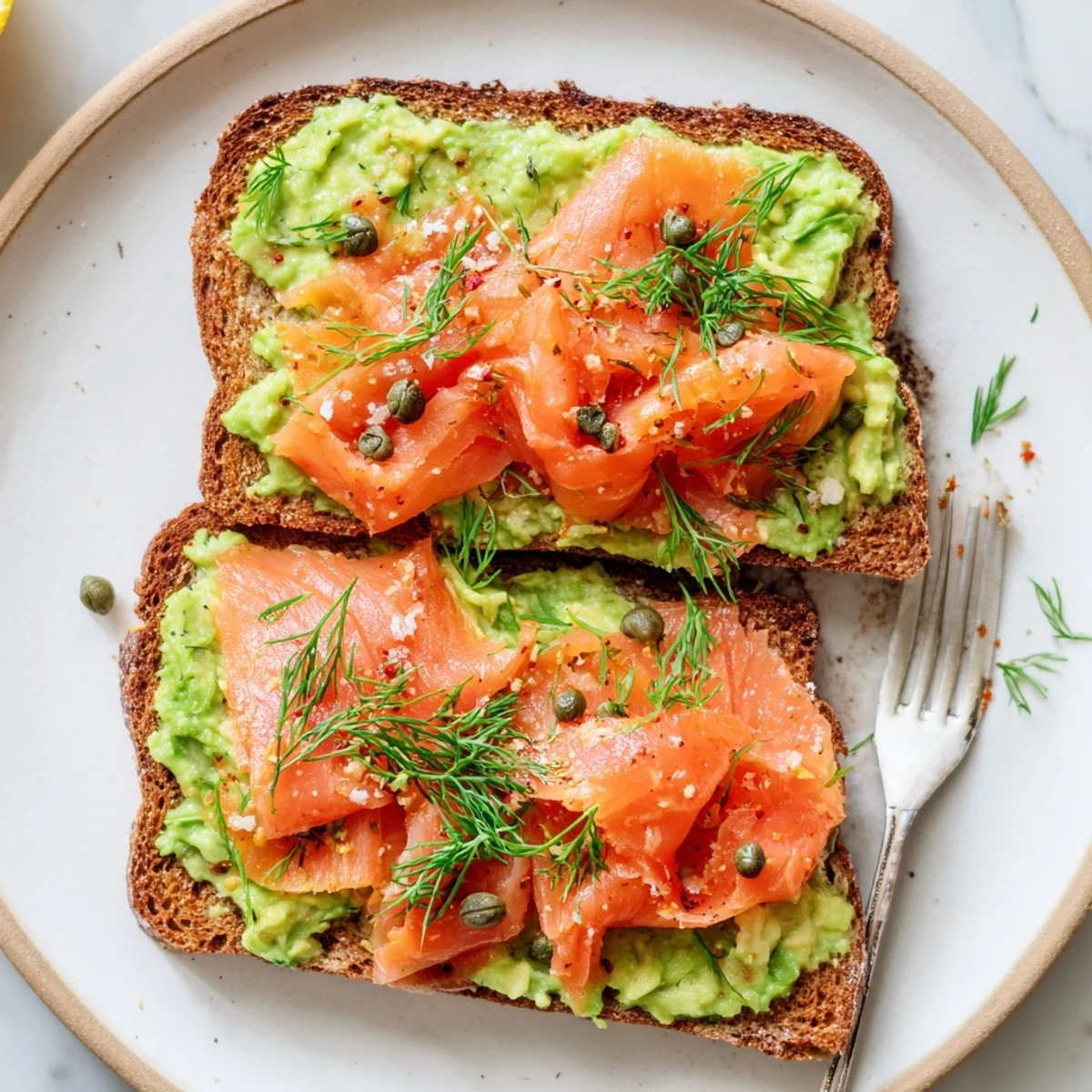 Salmon Avocado Toast garnished with capers, red pepper flakes, optional poached egg.