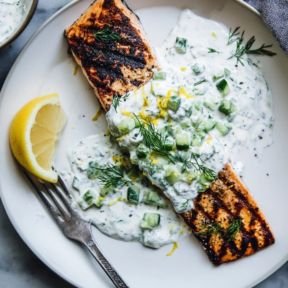 Golden grilled salmon fillets with char marks drizzled with creamy cucumber dill yogurt sauce