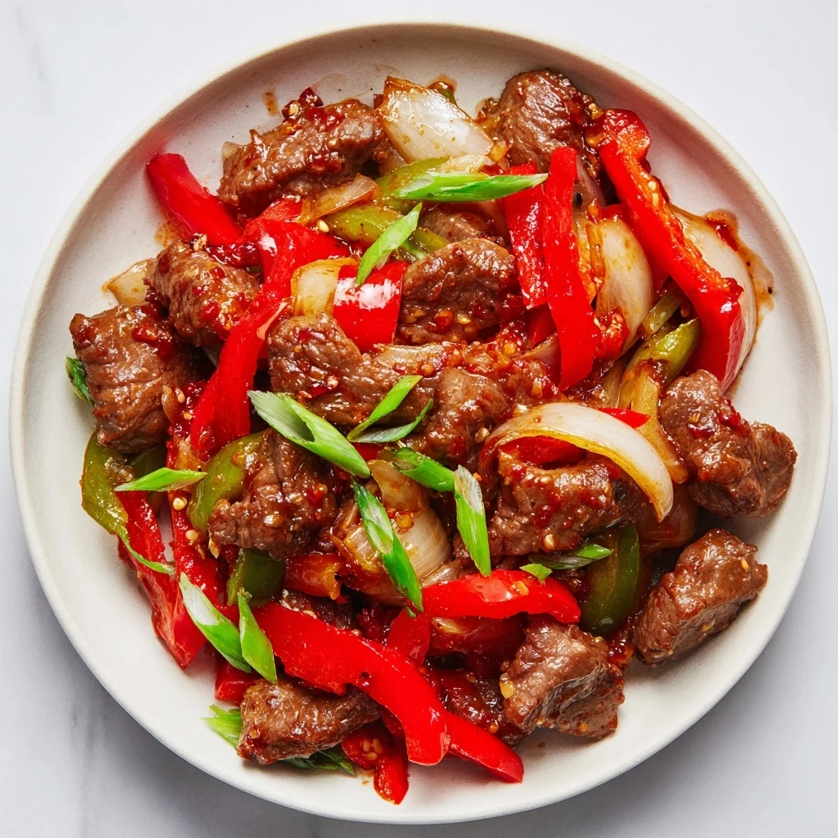 Spicy beef stir fry with chili garlic plated with crisp vegetables and garnished fresh green onions
