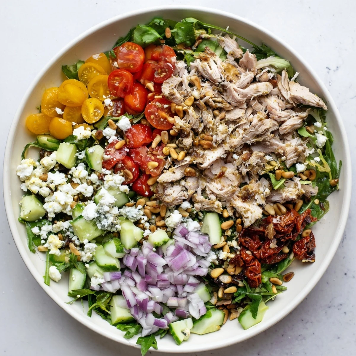 Fresh sun dried tomato chicken salad with tender chicken, crisp veggies, and crumbled feta cheese in a large bowl
