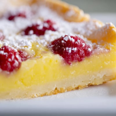 Tangy lemon raspberry bars on white plate dusted with powdered sugar topping