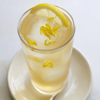 Sunlit glass of Dandelion Lemonade Recipe garnished with lemon slice and petals