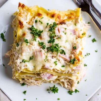 Chicken Cordon Bleu Lasagna slices revealing creamy white béchamel sauce between pasta sheets dotted with shredded chicken and ham